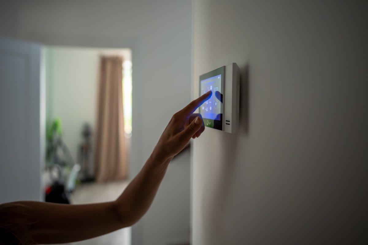 Closeup hand using smart home touch screen with connected appliances device on wall. Setting, checking energy security heating system on digital control in apartment. Home automation monitoring.