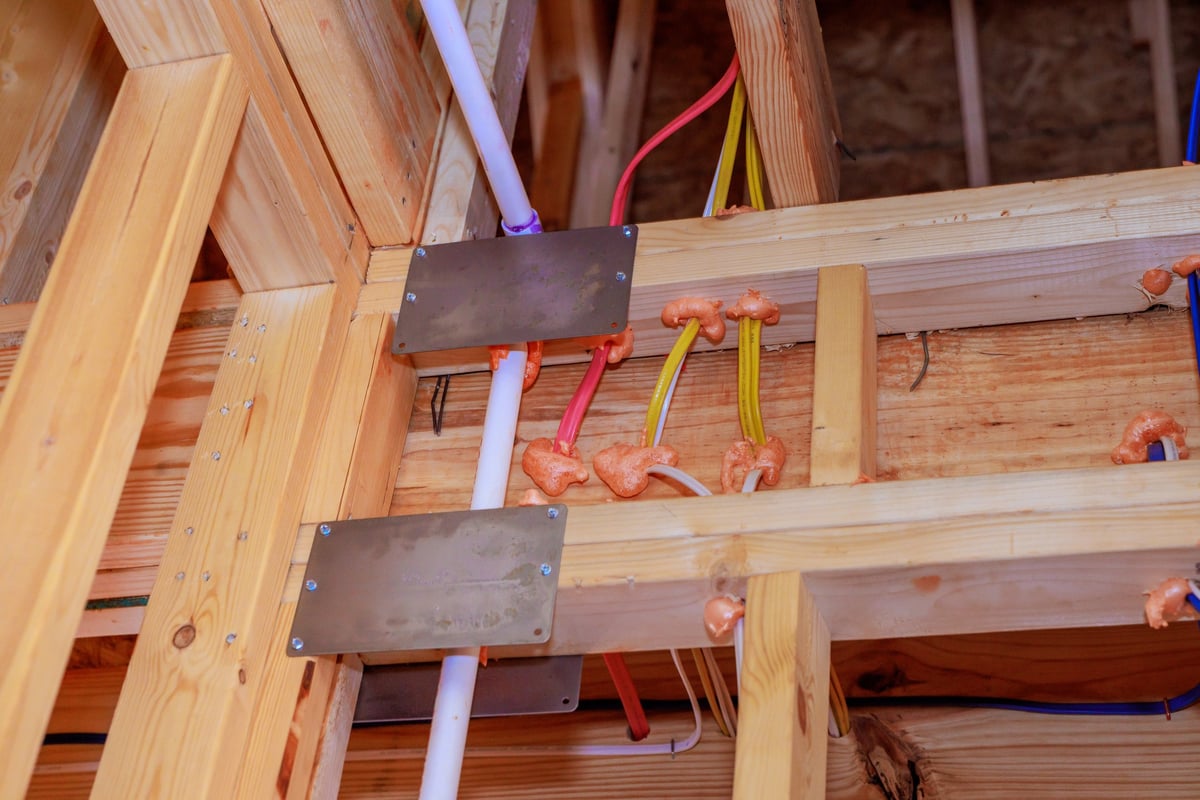 Construction site features electrical wires, plumbing pipes secured to wooden beams in new building