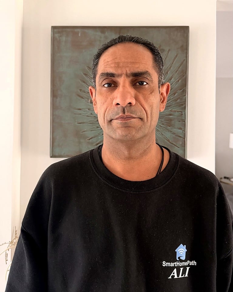 Portrait of a middle-aged man wearing a black SmartHomePath Ali sweatshirt, standing in front of an artwork with a textured background